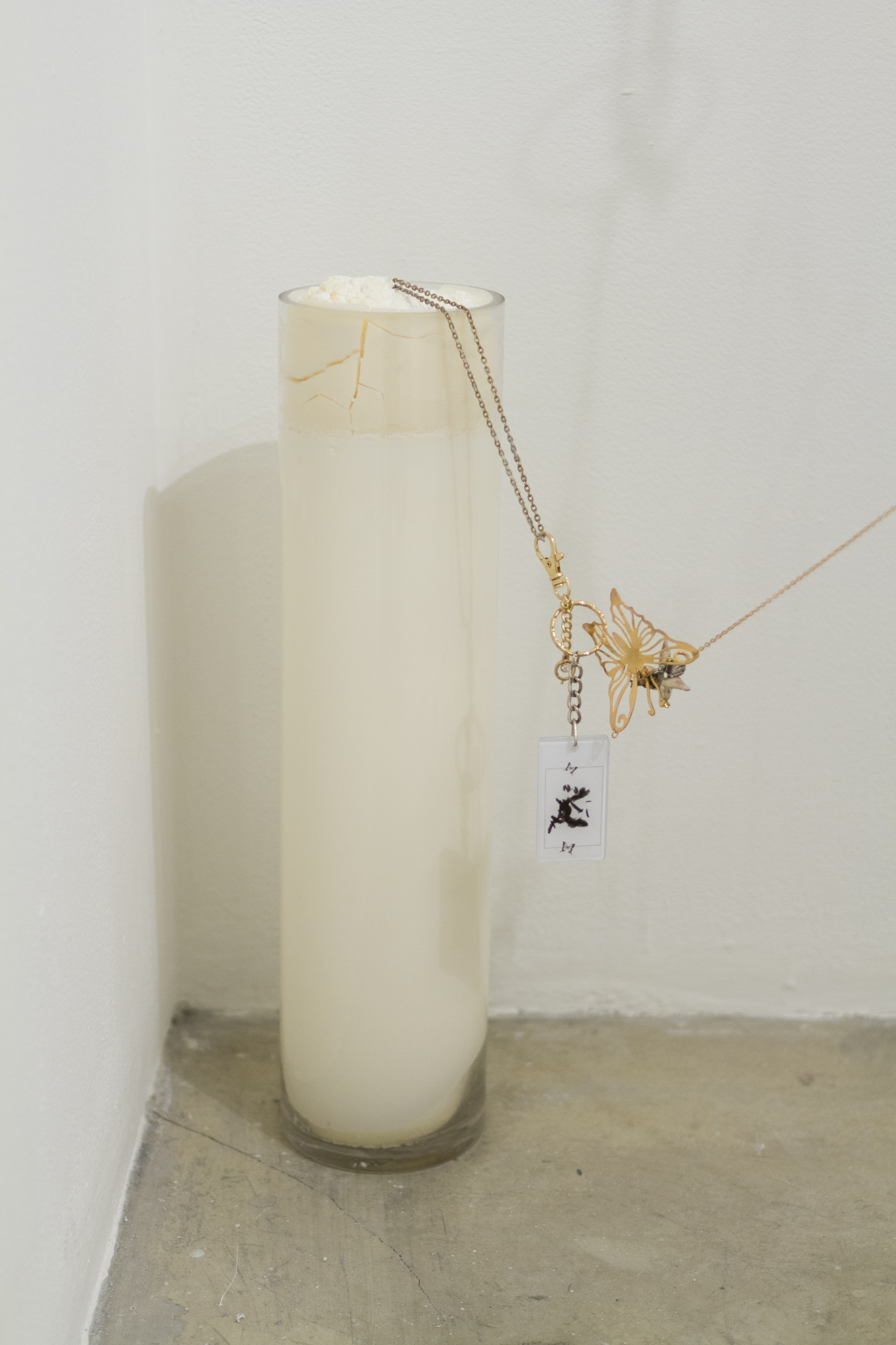 A glass column filled with white wax with delicate charms and chains attached to it